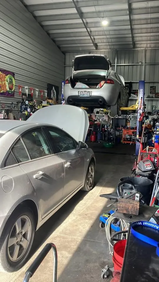 Shop interior — two vehicles on lifts (sedan + hatchback), equipment and banners visible.